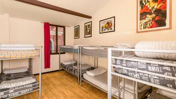 A dormitory room with bunk beds, wooden floors, and artwork on the walls.