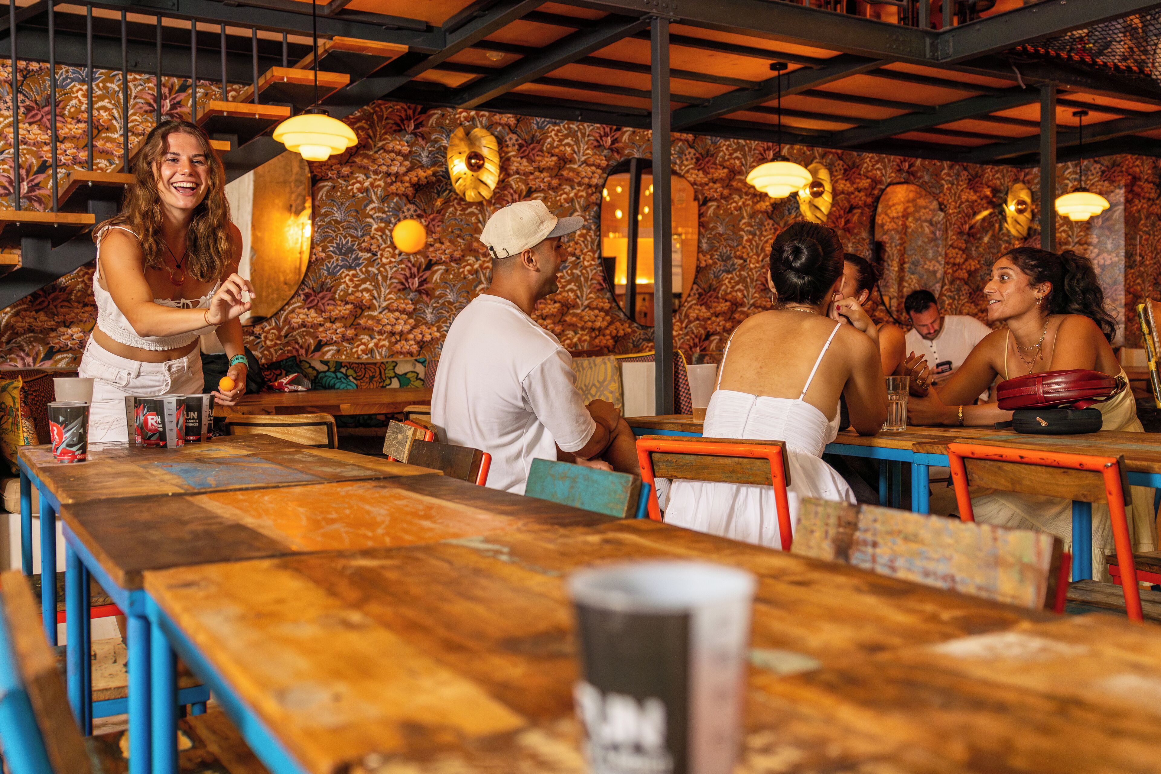 A restaurant with wooden tables and chairs, a patterned wall, and hanging lights.