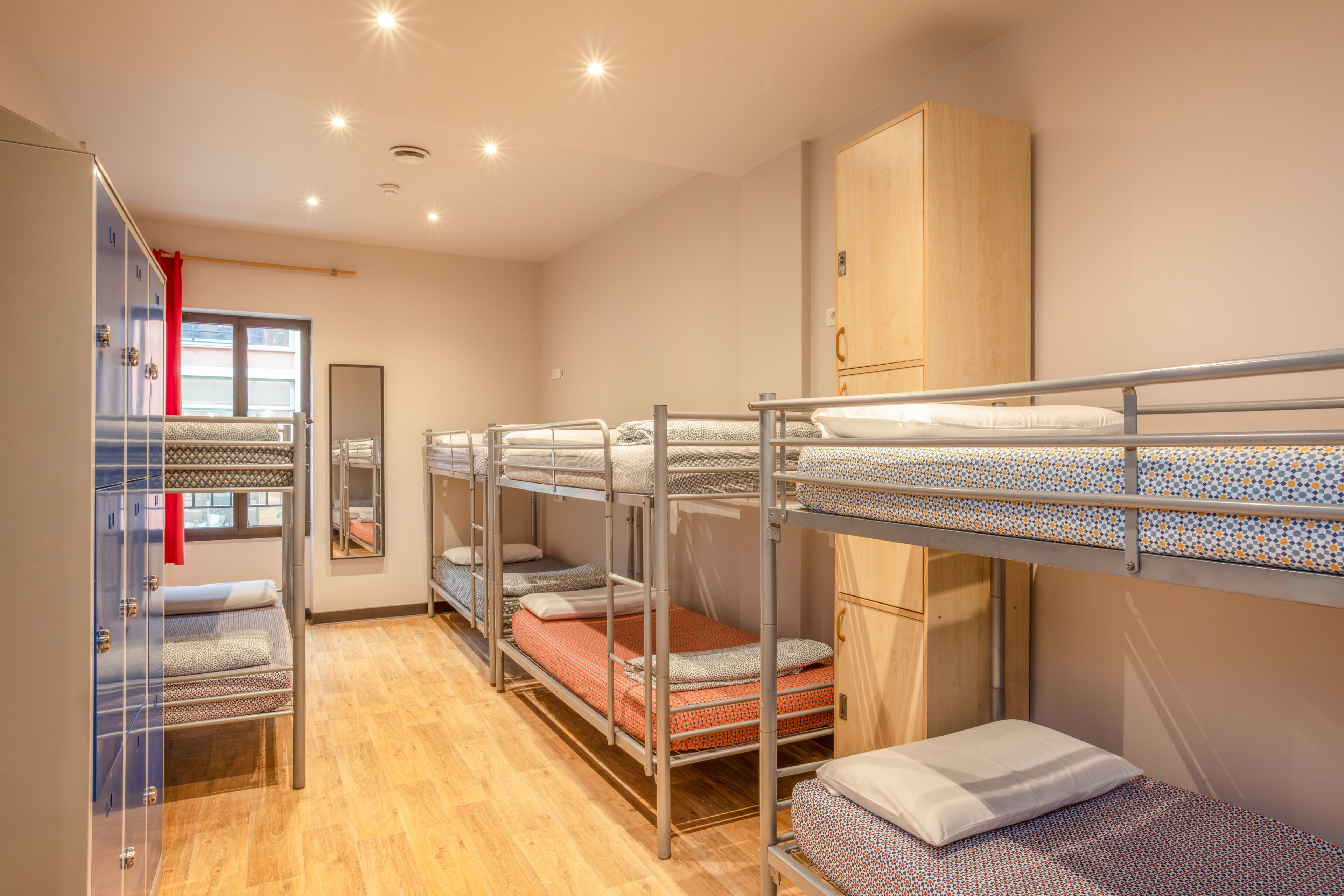 A dormitory room with bunk beds, a wardrobe, and a mirror.