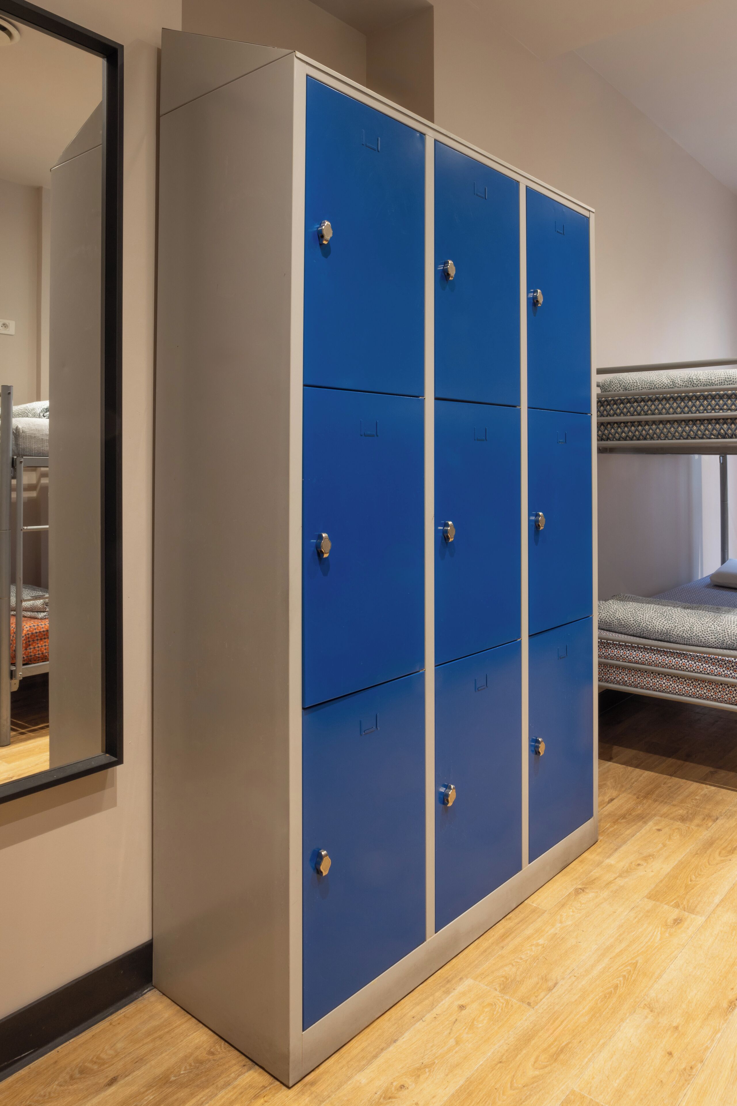 A room with a bunk bed, a large wardrobe with multiple compartments, and a mirror on the wall.