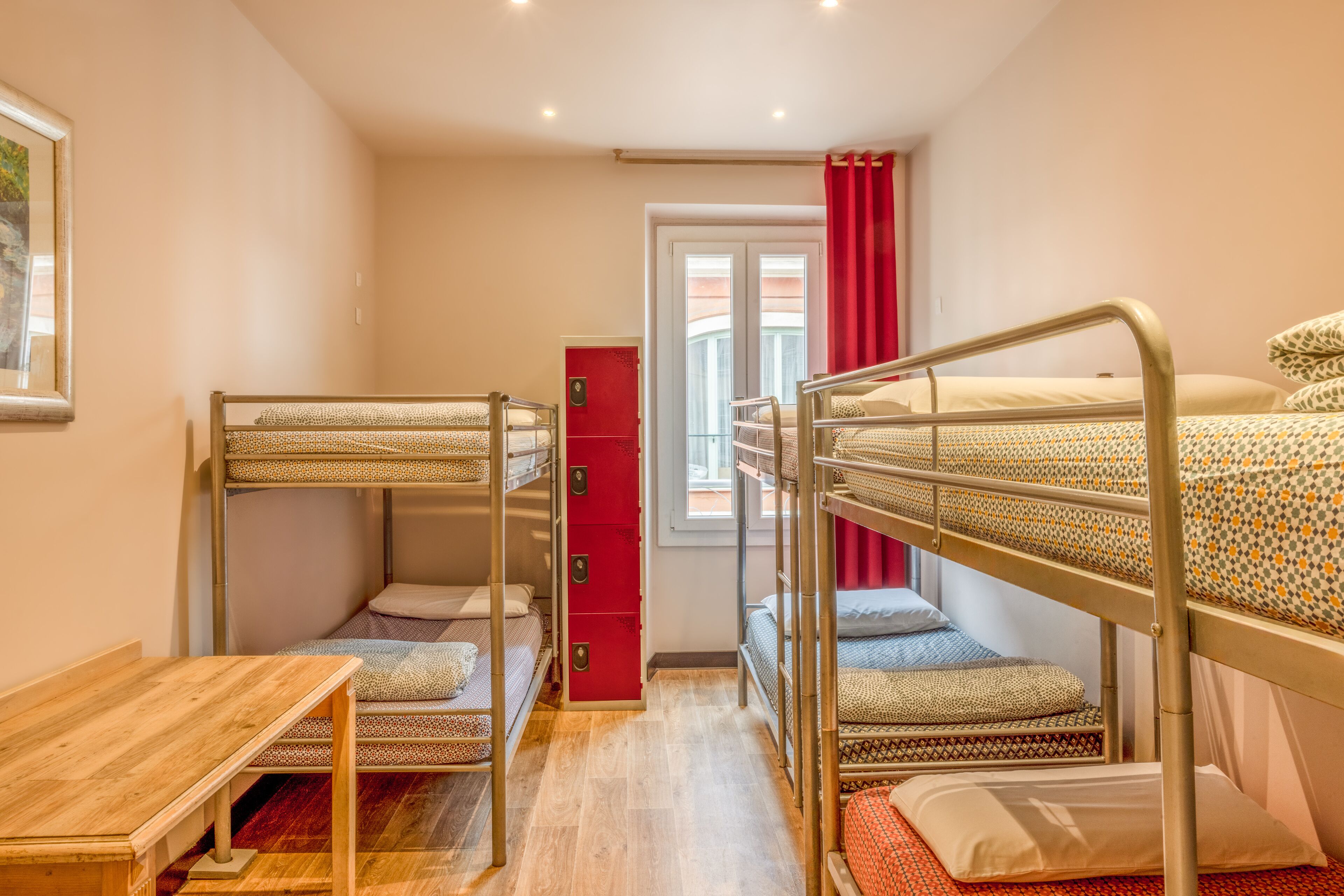 A dormitory room with bunk beds, a wooden table, and a red cabinet.