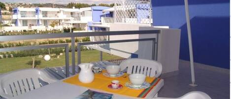 Un balcón con una mesa lista para dos personas, una revista y una jarrón.