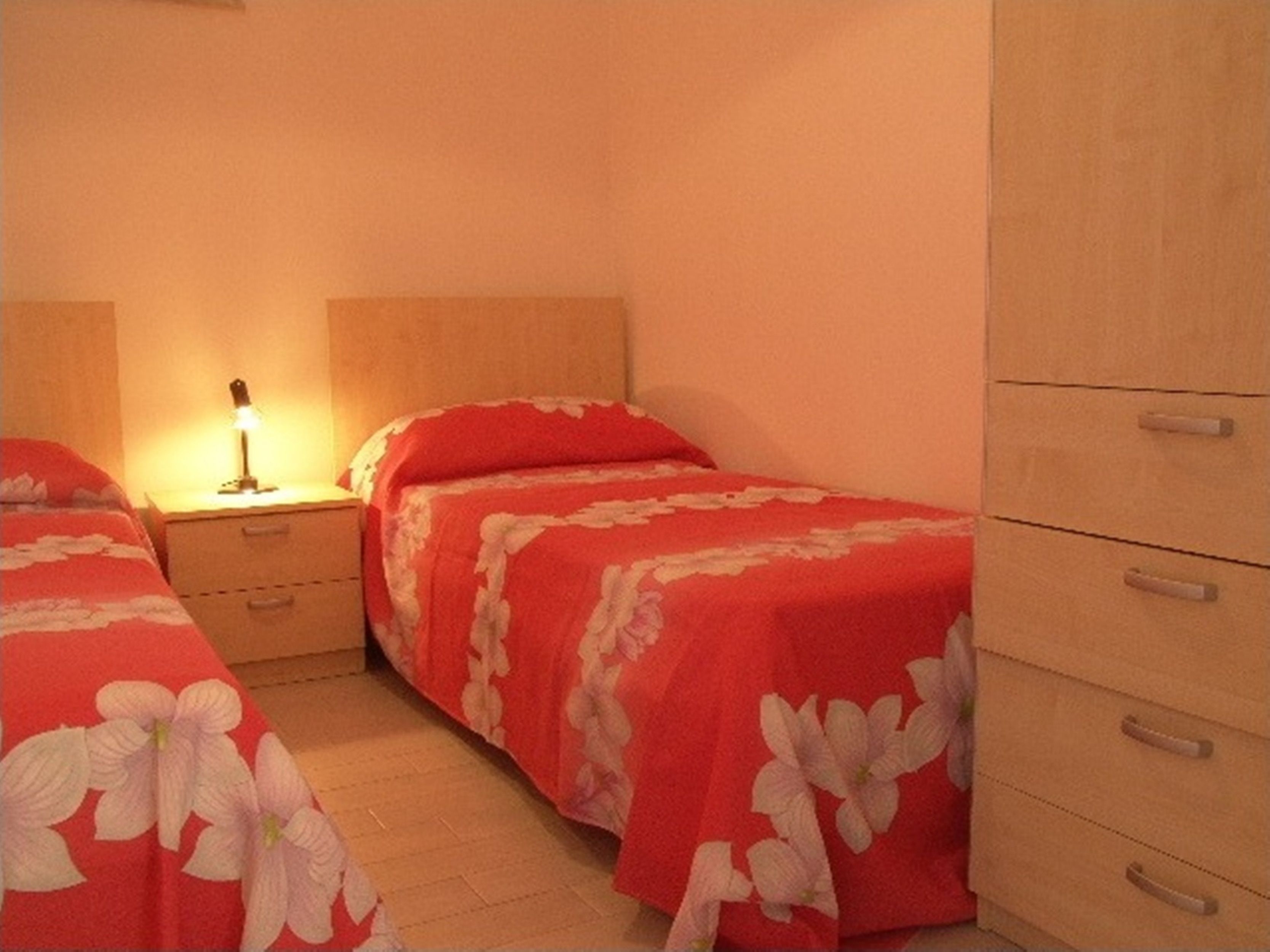 Quarto com duas camas, mesa de cabeceira com abajur e guarda-roupa.