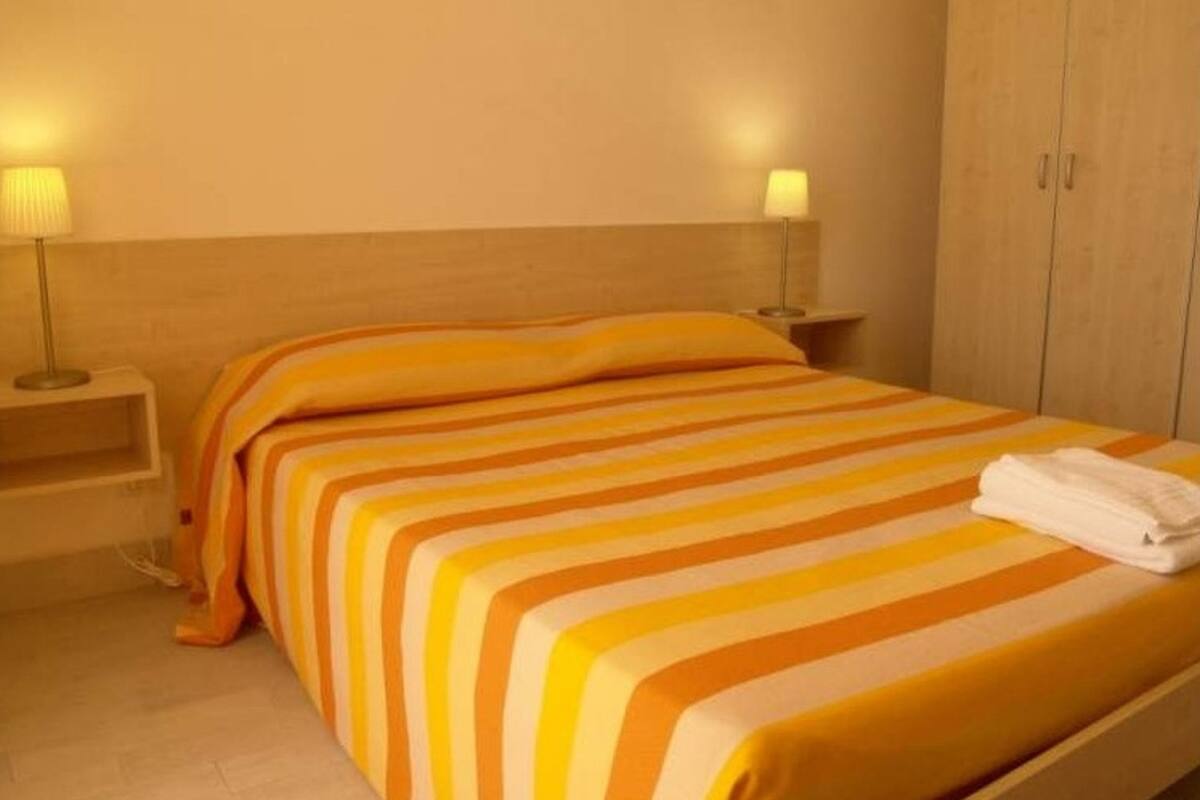 A hotel room with a bed, two bedside lamps, and a wardrobe.