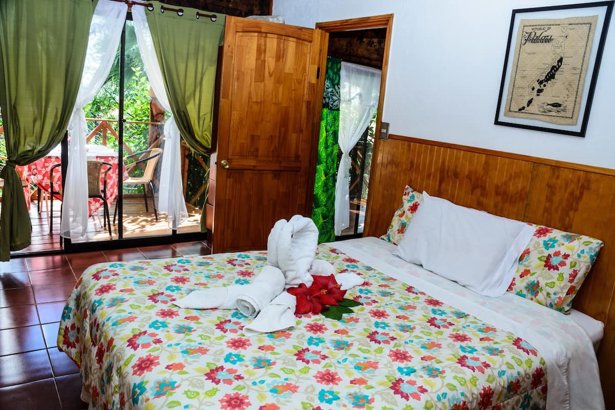 Een hotelkamer met een bed, een bloemenprint sprei, een lijst met een kaart aan de muur en een schuifdeur naar een buitenruimte.