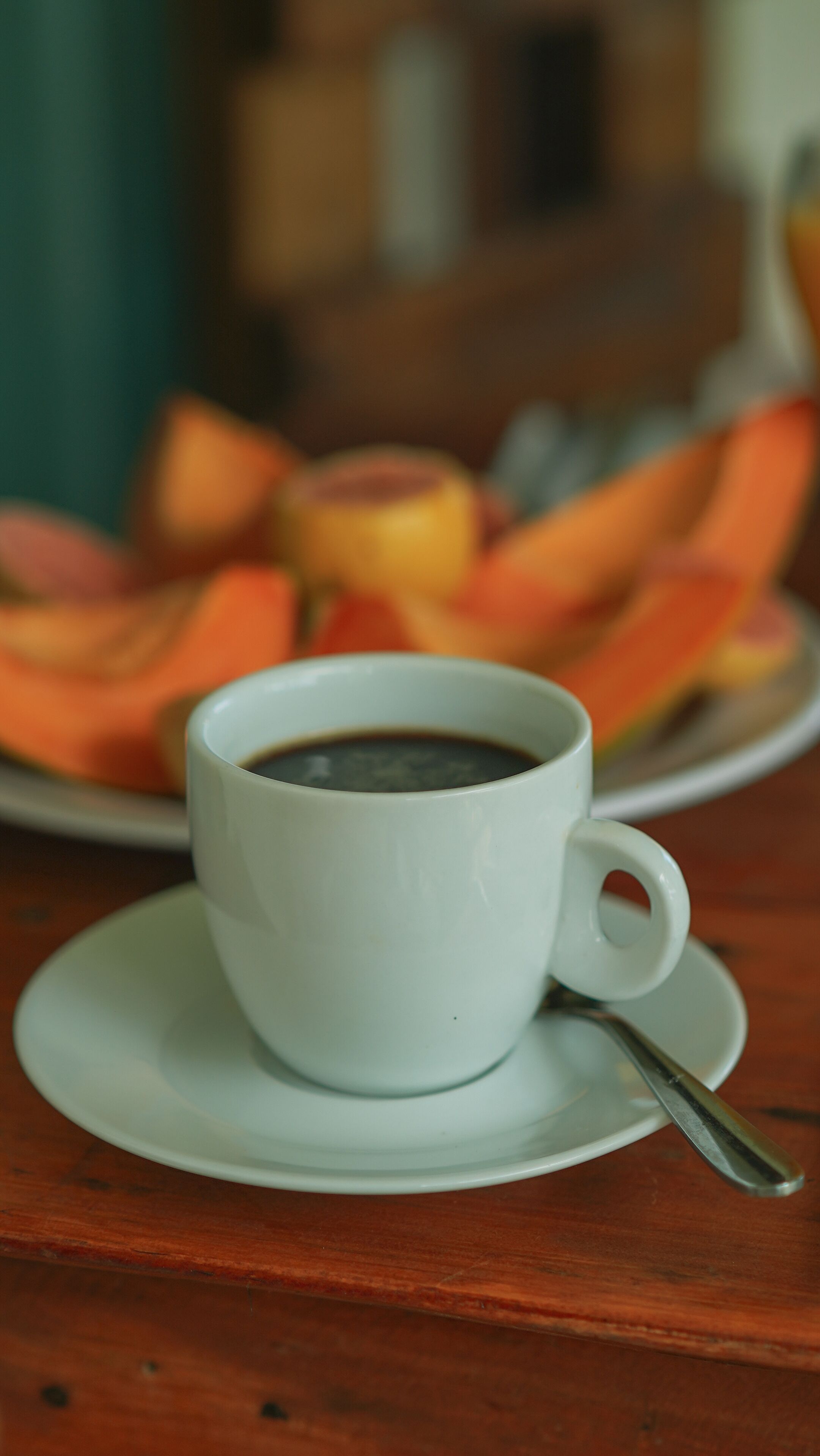 Una taza de café blanca sobre un plato, con una cuchara, colocada sobre una mesa de madera.