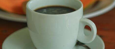 Una taza de café blanca sobre un plato, con una cuchara, colocada sobre una mesa de madera.