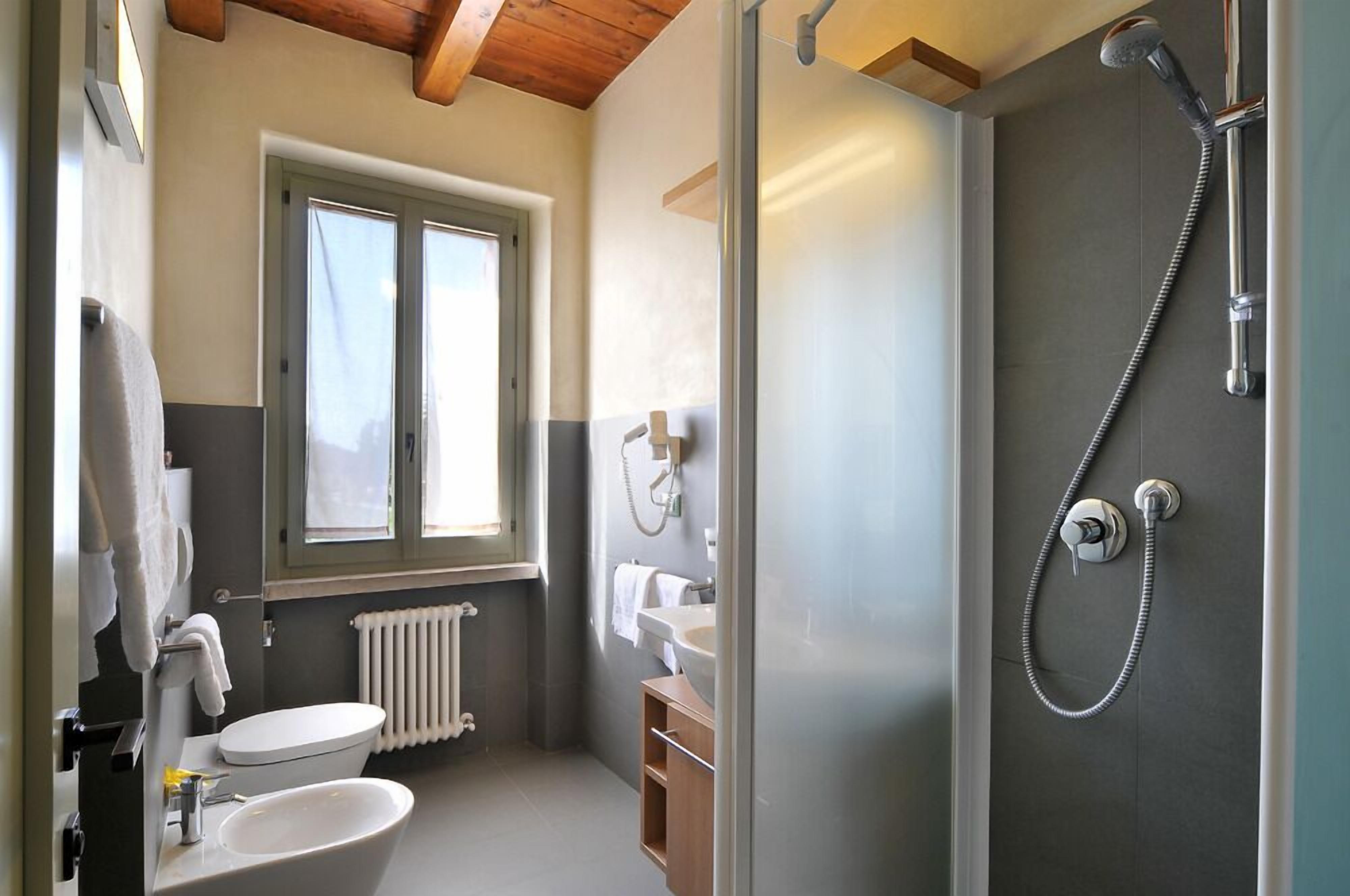 A compact bathroom with a toilet, sink, and shower. There is a window providing natural light and a radiator below the window.