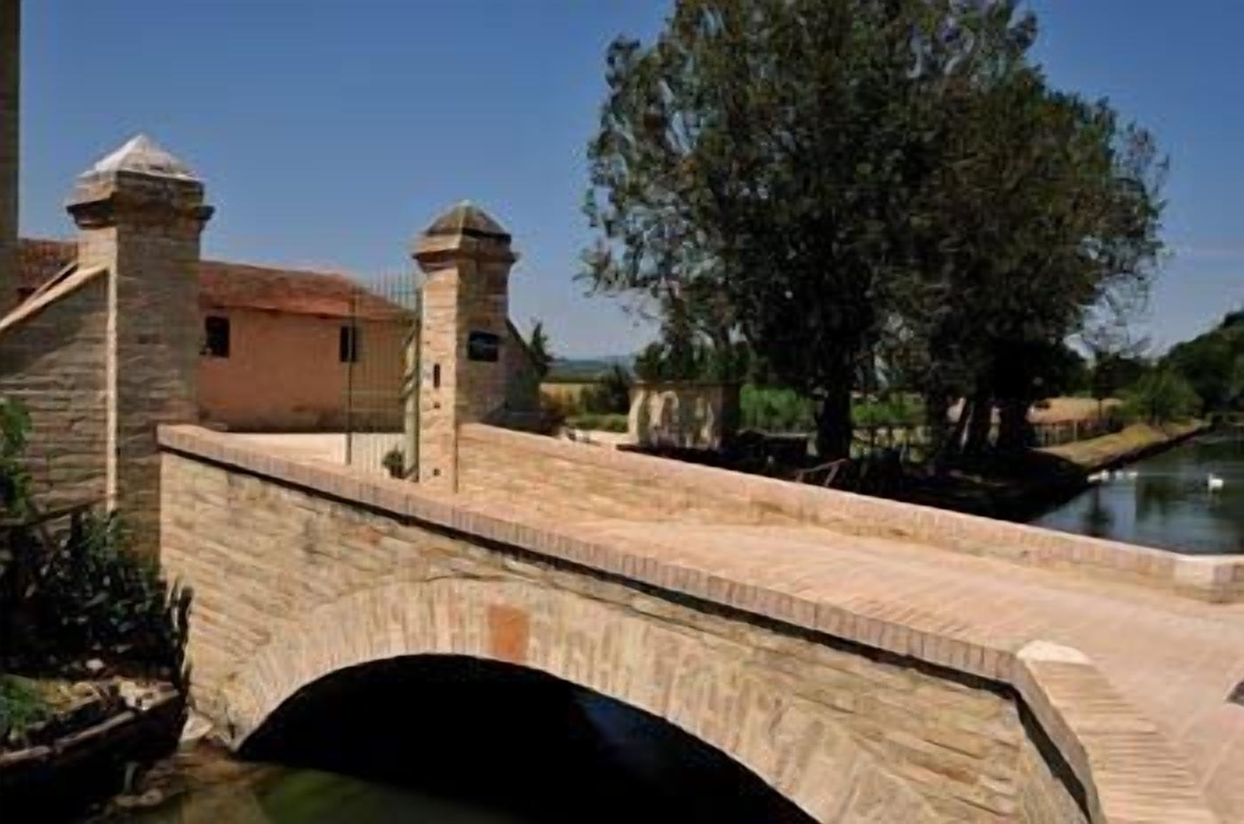 A stone bridge with two towers, a small building, and a body of water.