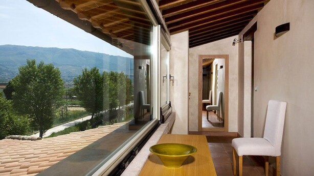 Une chambre moderne dotée d’une grande fenêtre donnant sur un paysage pittoresque, d’une table en bois avec un bol, et d’une chaise blanche.