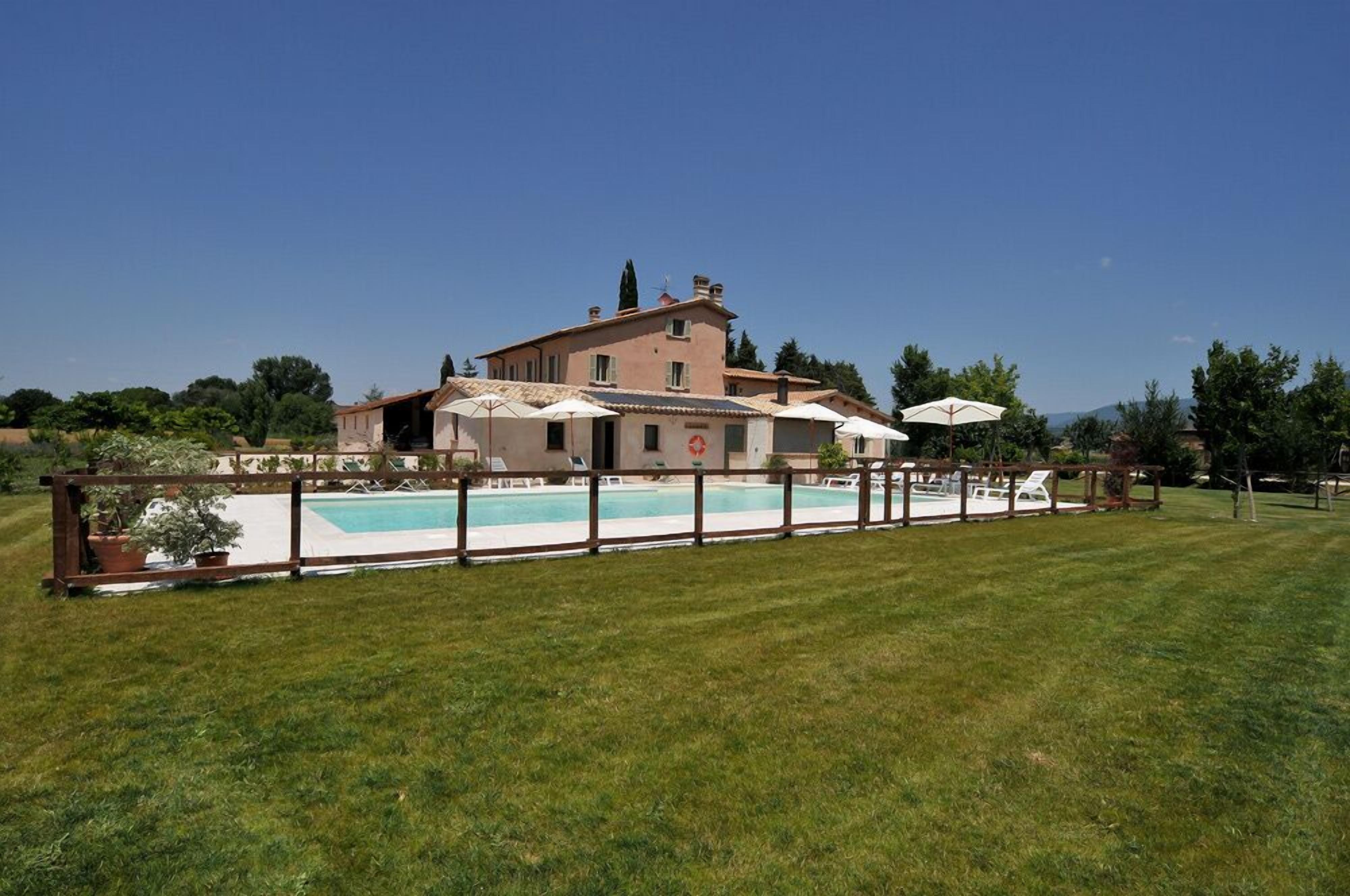 A large house with a swimming pool, surrounded by a wooden fence and several umbrellas.