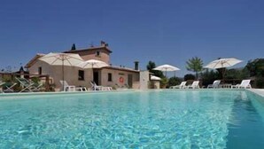 Une piscine d’un bleu éclatant, entourée de chaises longues et de parasols, un bâtiment sur lequel est affiché un panneau représentant une bouée de sauvetage, et un ciel dégagé.