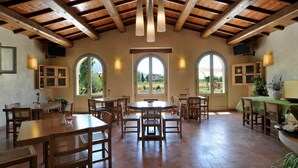 Un vaste espace dédié à la salle à manger, avec des tables et des chaises en bois, de grandes fenêtres en arc de cercle et un haut plafond également en bois.