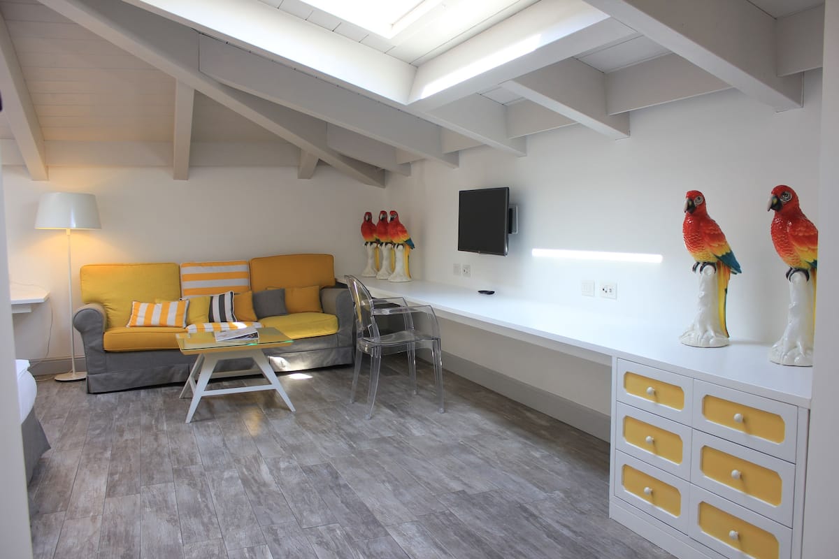 Un salon moderne avec un canapé, des chaises transparentes, une table basse et un téléviseur fixé au mur.