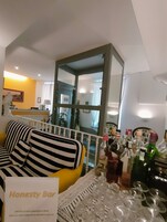 A bar area with a striped sofa, a glass partition, and a variety of bottles and glasses.