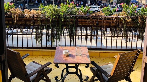 Una terraza con dos sillas de madera y una mesa, con vistas a una calle con edificios y un canal.