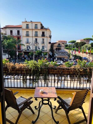 Una terraza con dos sillas de madera y una mesa, con vistas a una calle con edificios y un canal.