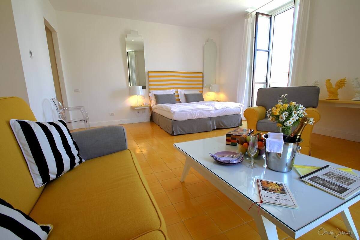 Une chambre d’hôtel avec un lit, un canapé jaune, une table basse en verre et un bureau avec une chaise.