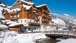 Un immeuble en bois à plusieurs étages, doté de balcons, entouré de montagnes enneigées et traversé par une rivière.