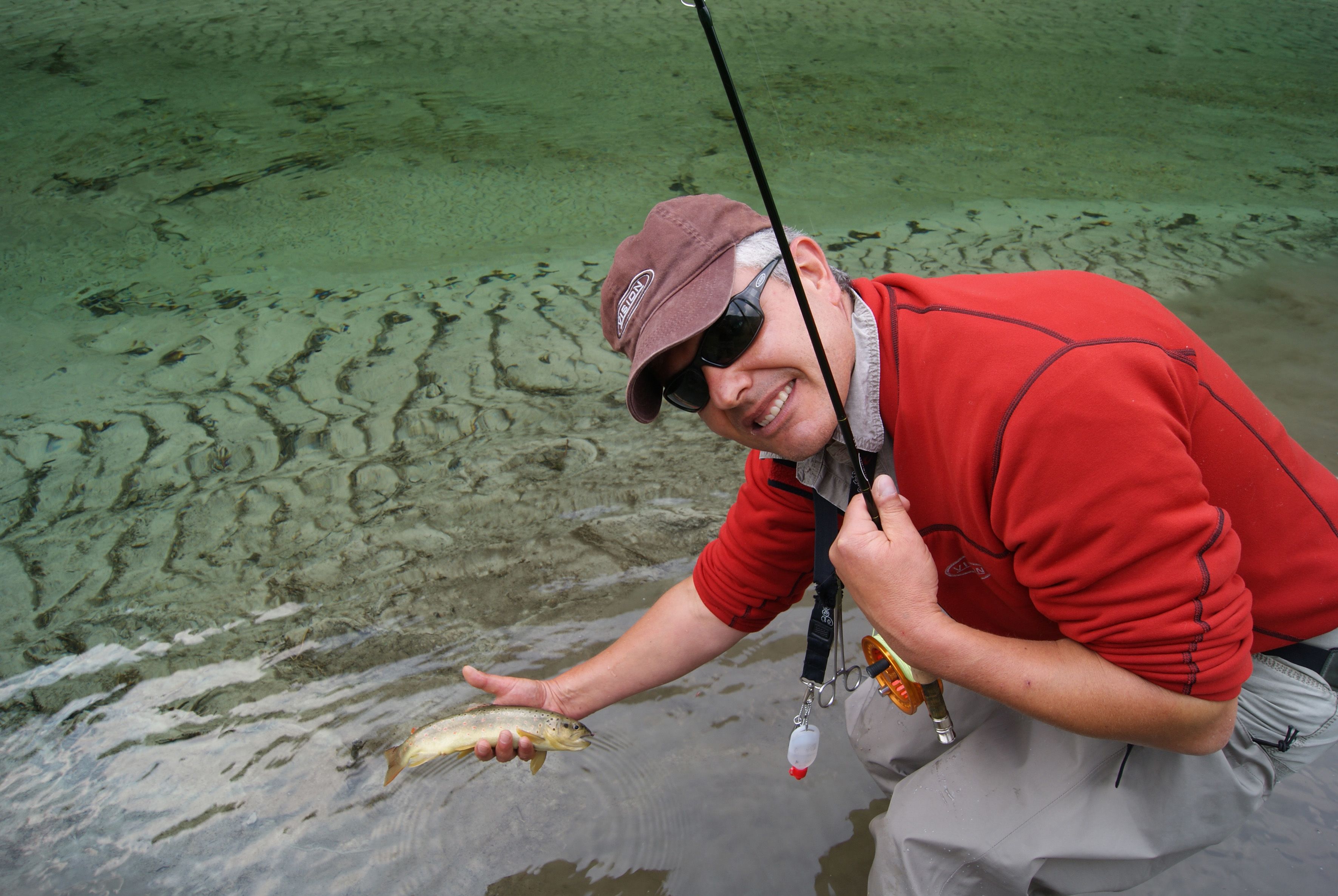 A person holding a fish near a body of water.