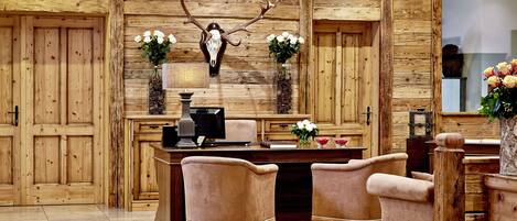 Een rustiek interieur met houten wanden, een bureau met twee stoelen en een gewei van een hert op de muur.