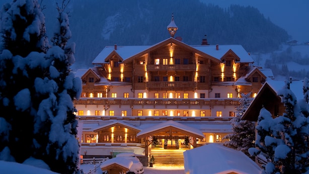 Un grand bâtiment en bois à plusieurs étages, doté de balcons et d’un éclairage chaleureux, entouré d’arbres couverts de neige.