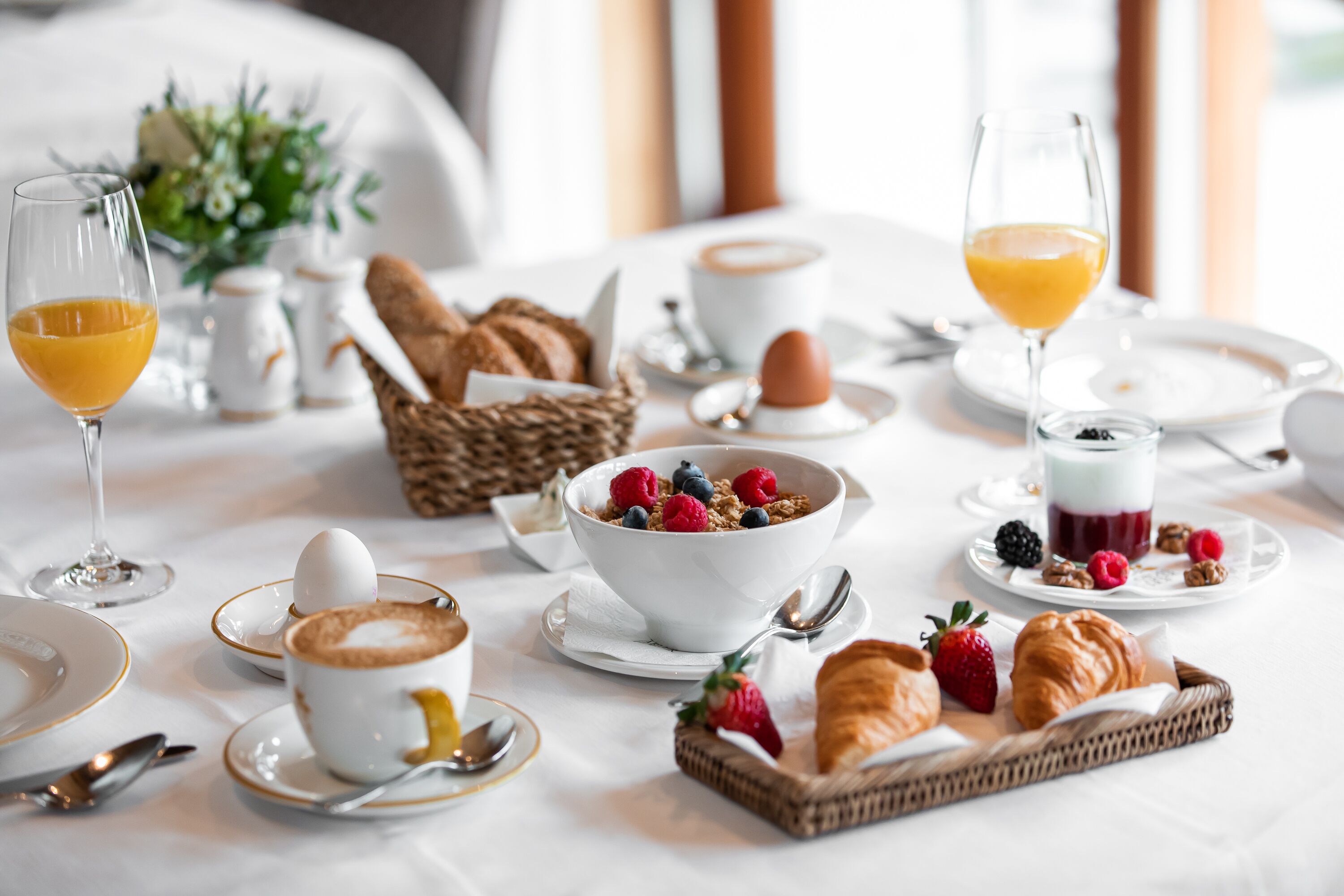 A breakfast setting with a variety of food items, including croissants, strawberries, and a bowl of cereal with berries.