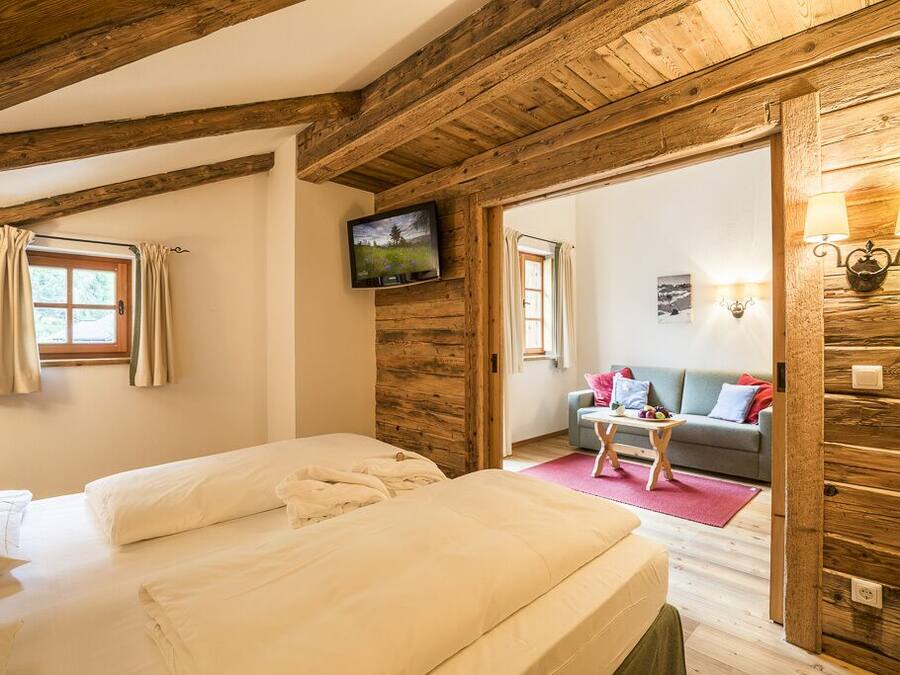 Una habitación acogedora con techo de madera, una cama, un televisor y un sofá con una mesita.