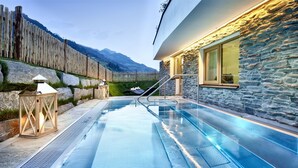 Une piscine bordée d’un muret en pierre et d’une clôture en bois, une chaise longue et une lanterne.