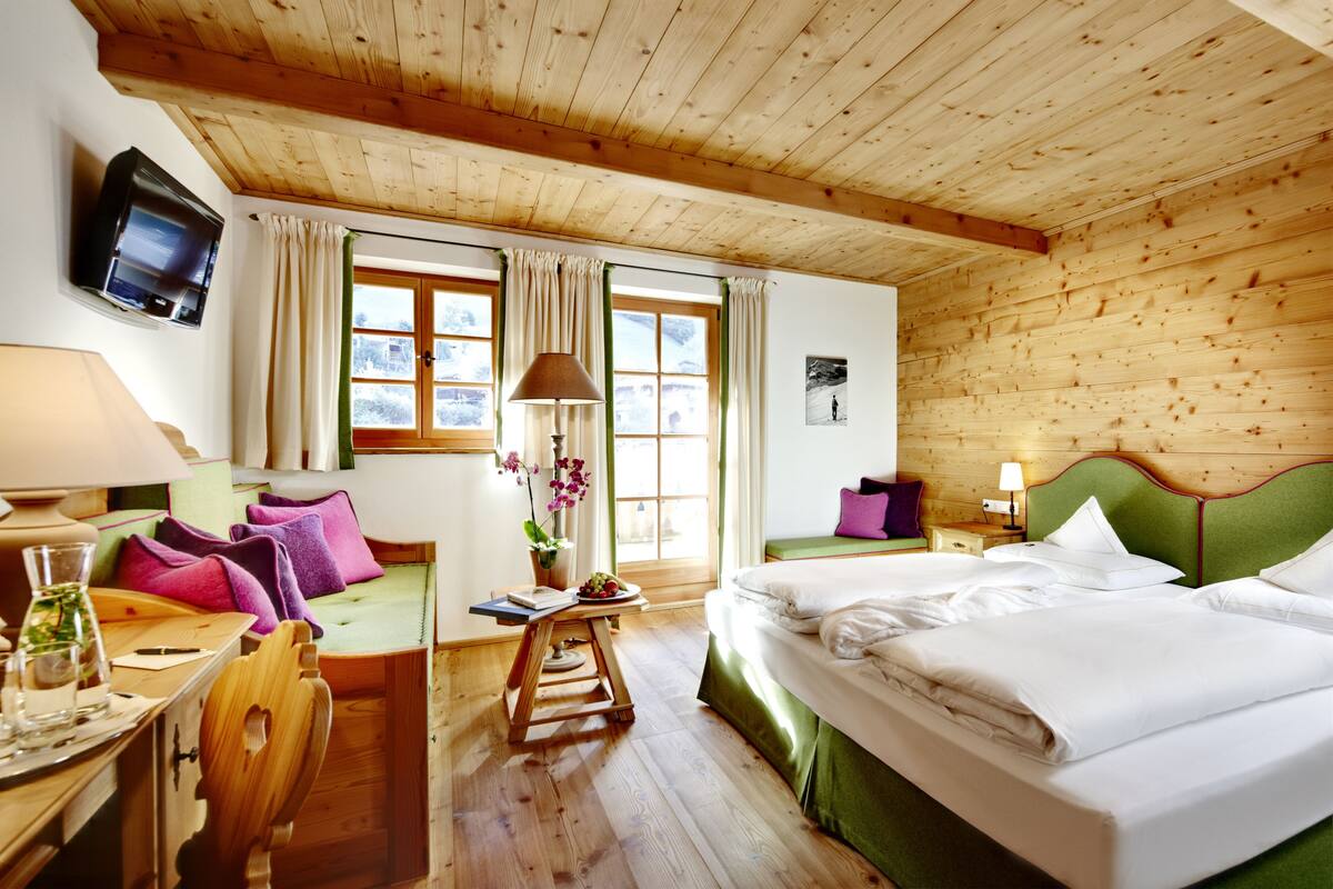 A wooden-paneled room with a bed, a desk, a chair, a TV, and a window with curtains.
