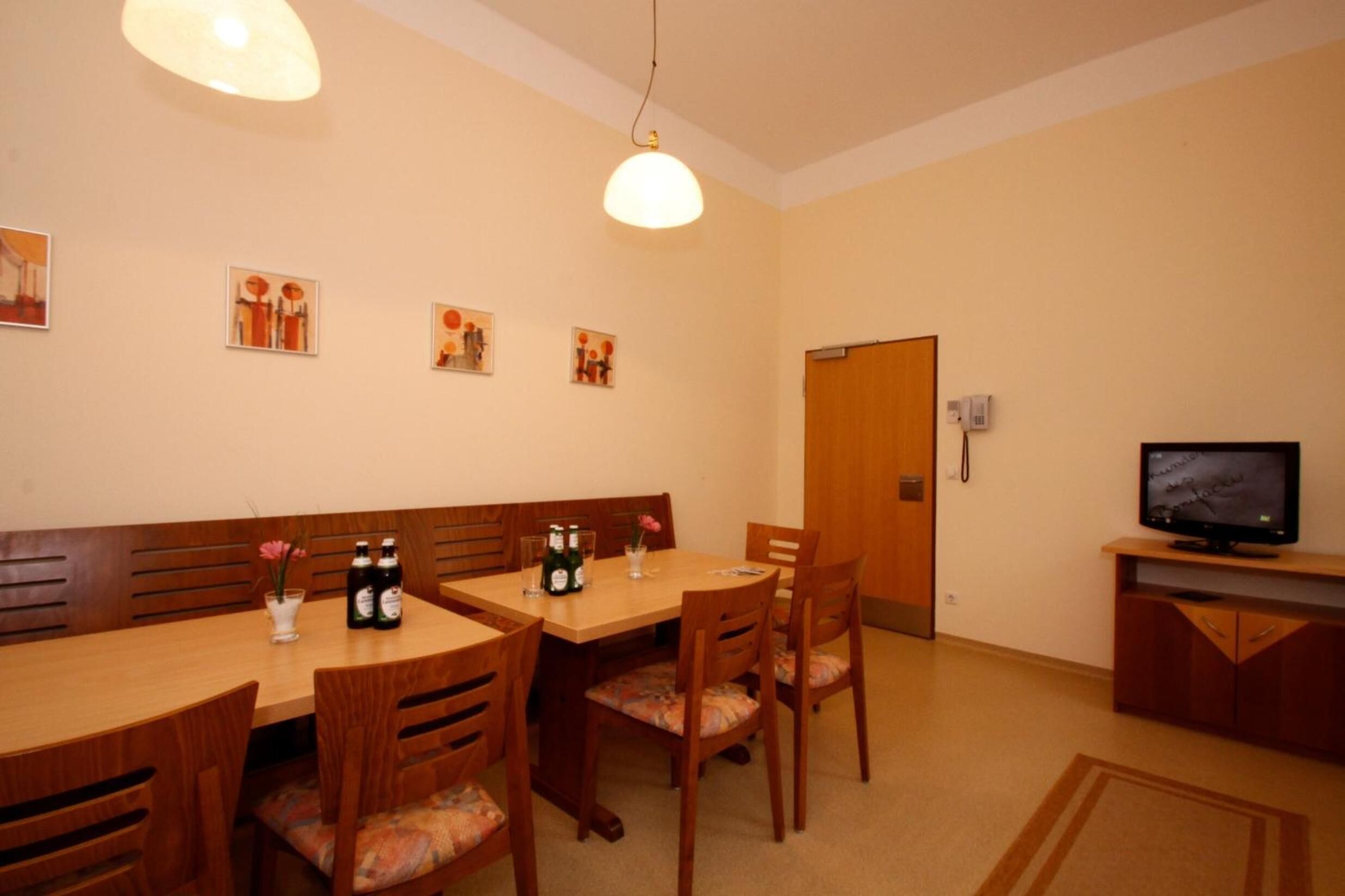A dining area with wooden tables and chairs, a television on a stand, and artwork on the wall.