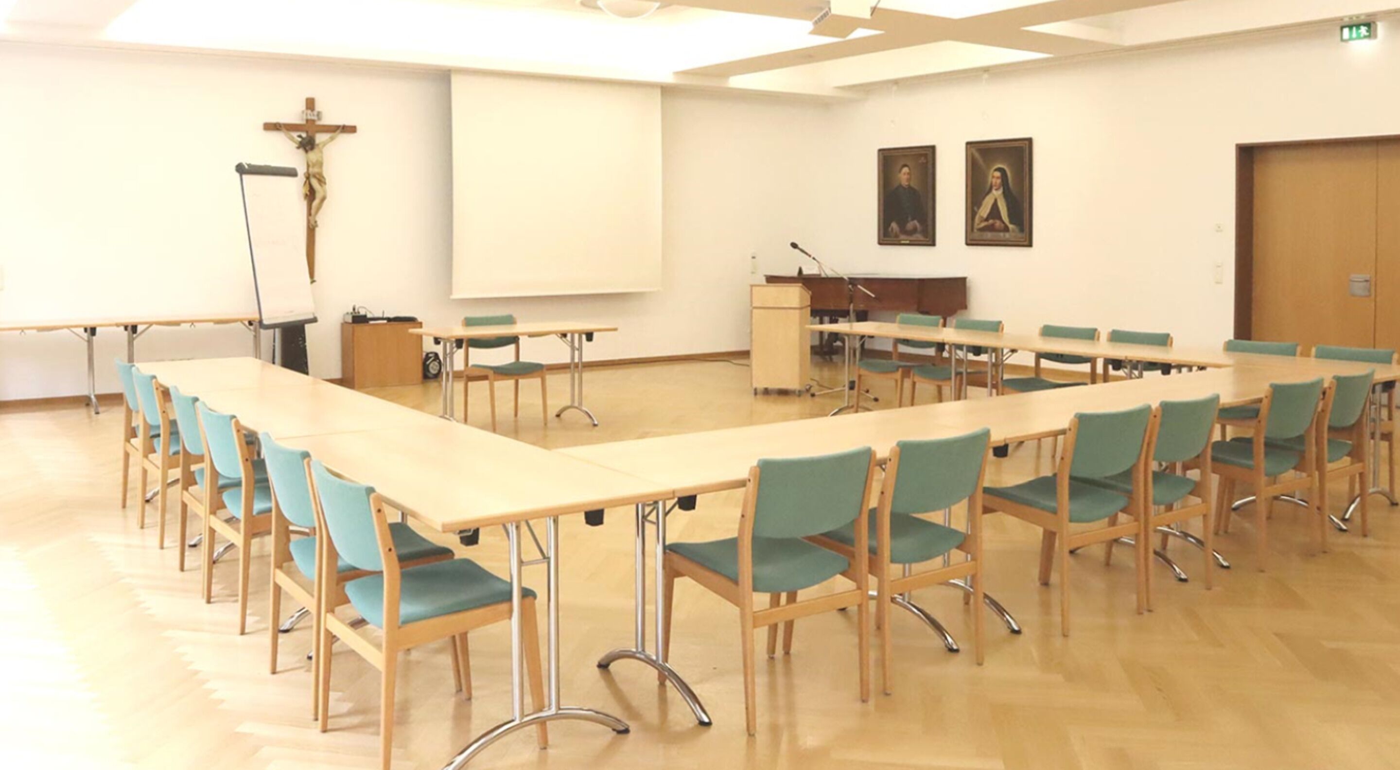 Una sala de conferències amb una taula llarga, cadires, un escenari i una pantalla de projector.