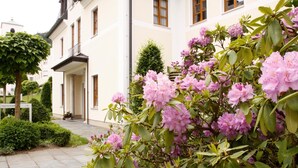 A building with a white facade, a balcony, and a garden with pink flowers.