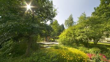 Um jardim com um gazebo, um lago e diversas plantas e flores.