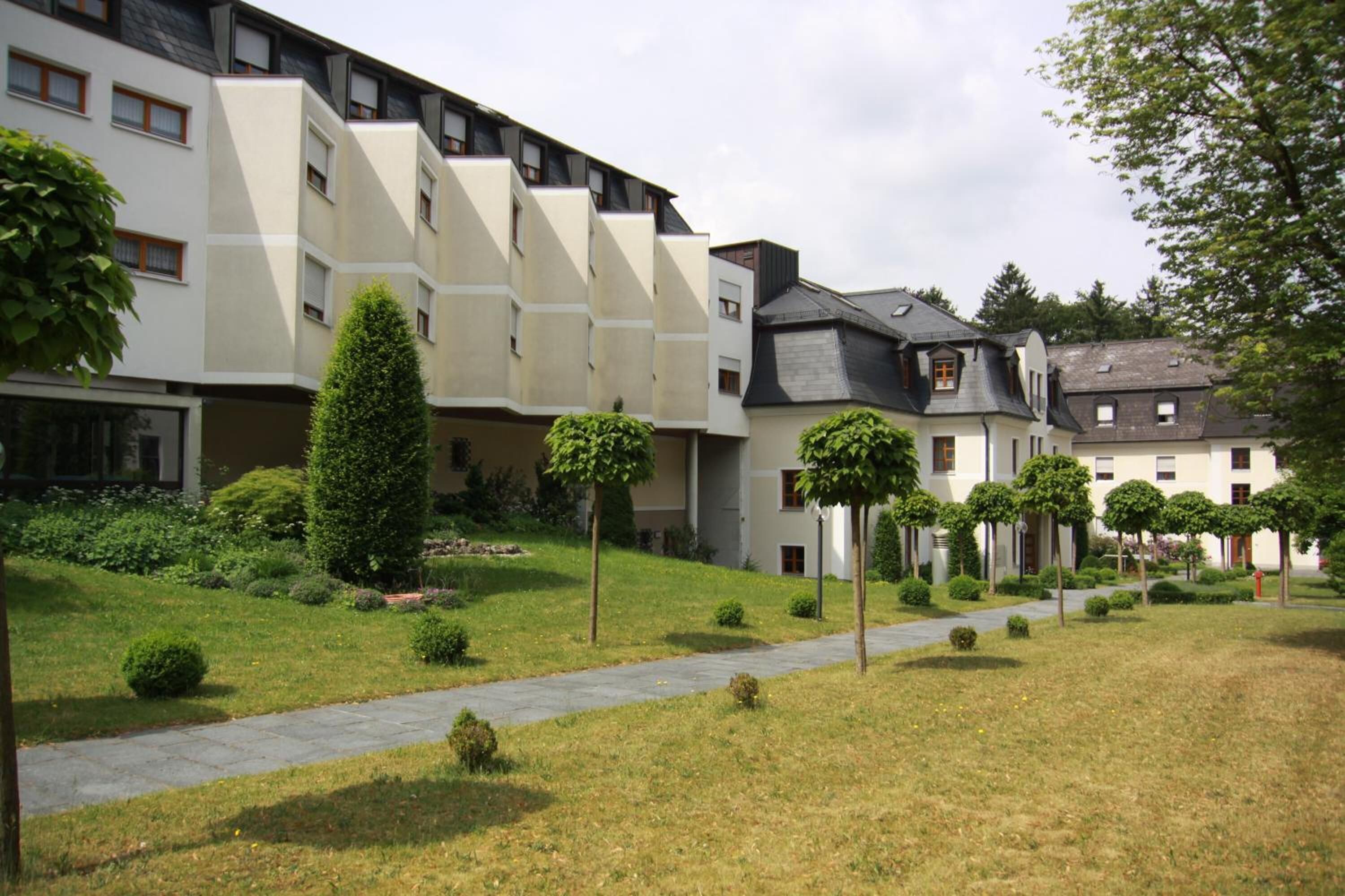 A modern building with multiple floors, a paved pathway, and well-maintained greenery.