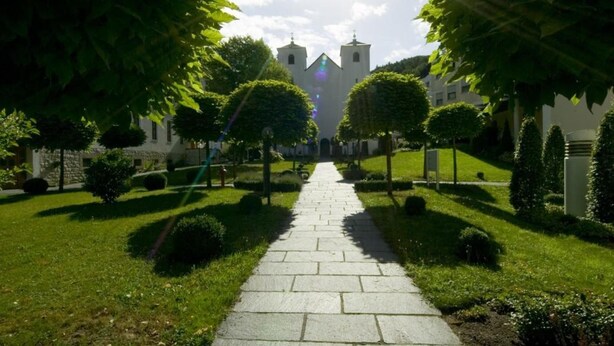 A pathway leading to a building with a tower, surrounded by well-maintained greenery and stone paving.