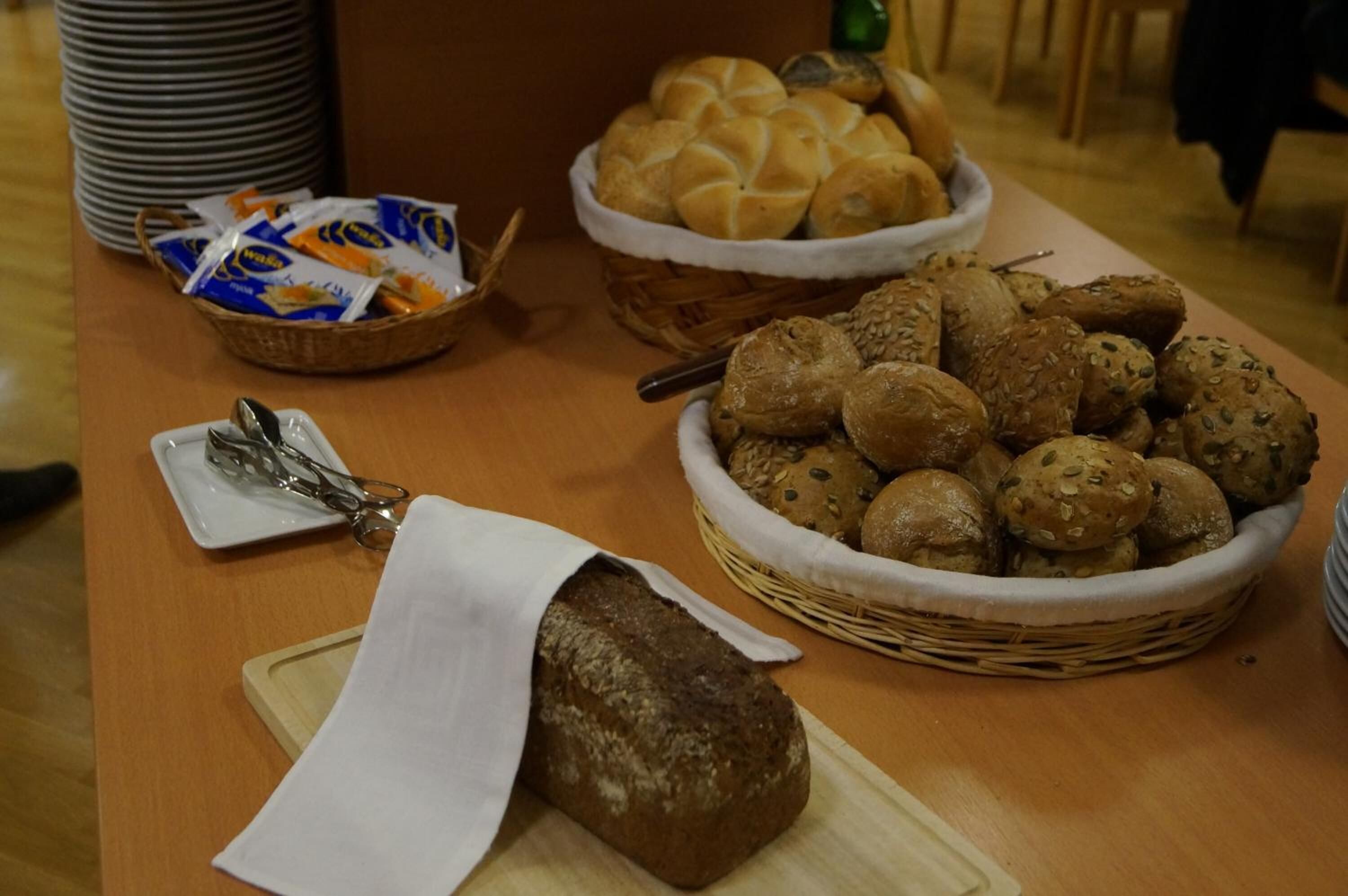 A table with various breads and pastries, including a loaf of bread on a cutting board and baskets of rolls and cookies.