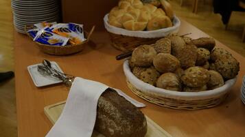 A table with various breads and pastries, including a loaf of bread on a cutting board and baskets of rolls and cookies.