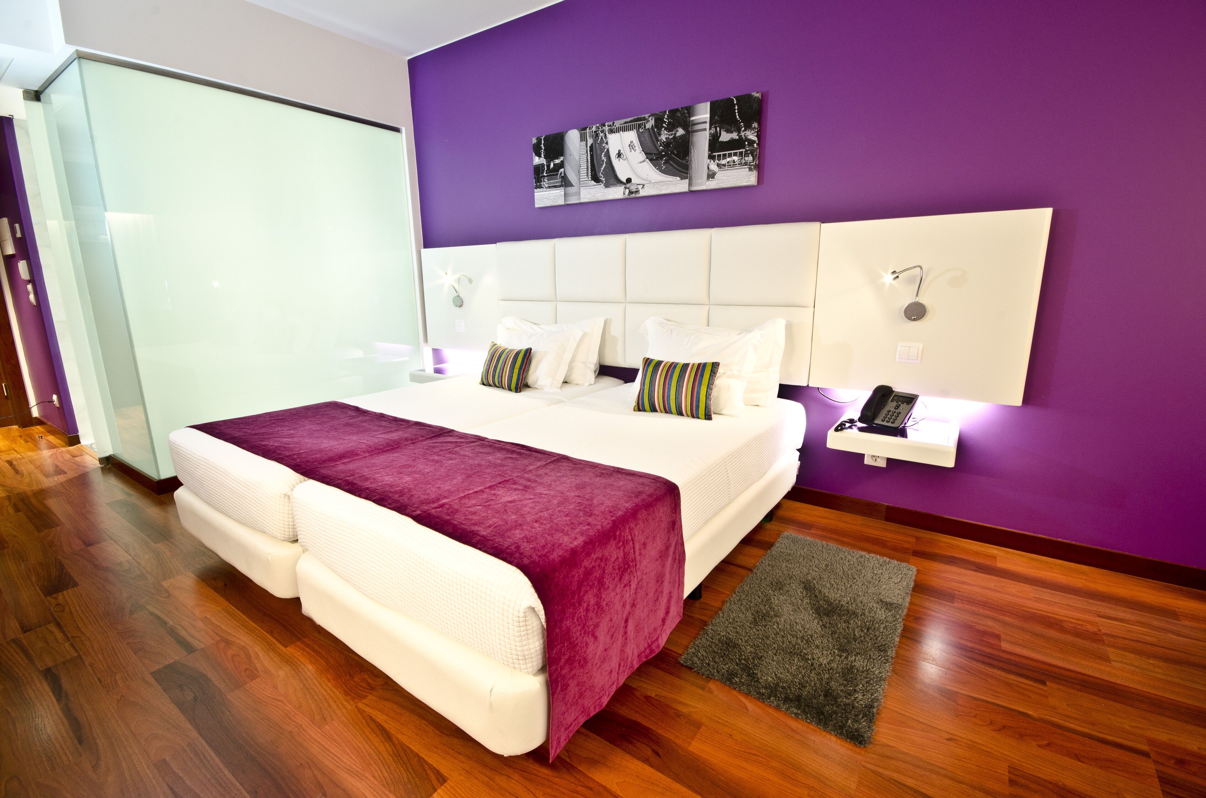 A modern bedroom with a large bed, a glass wardrobe, and a purple accent wall.