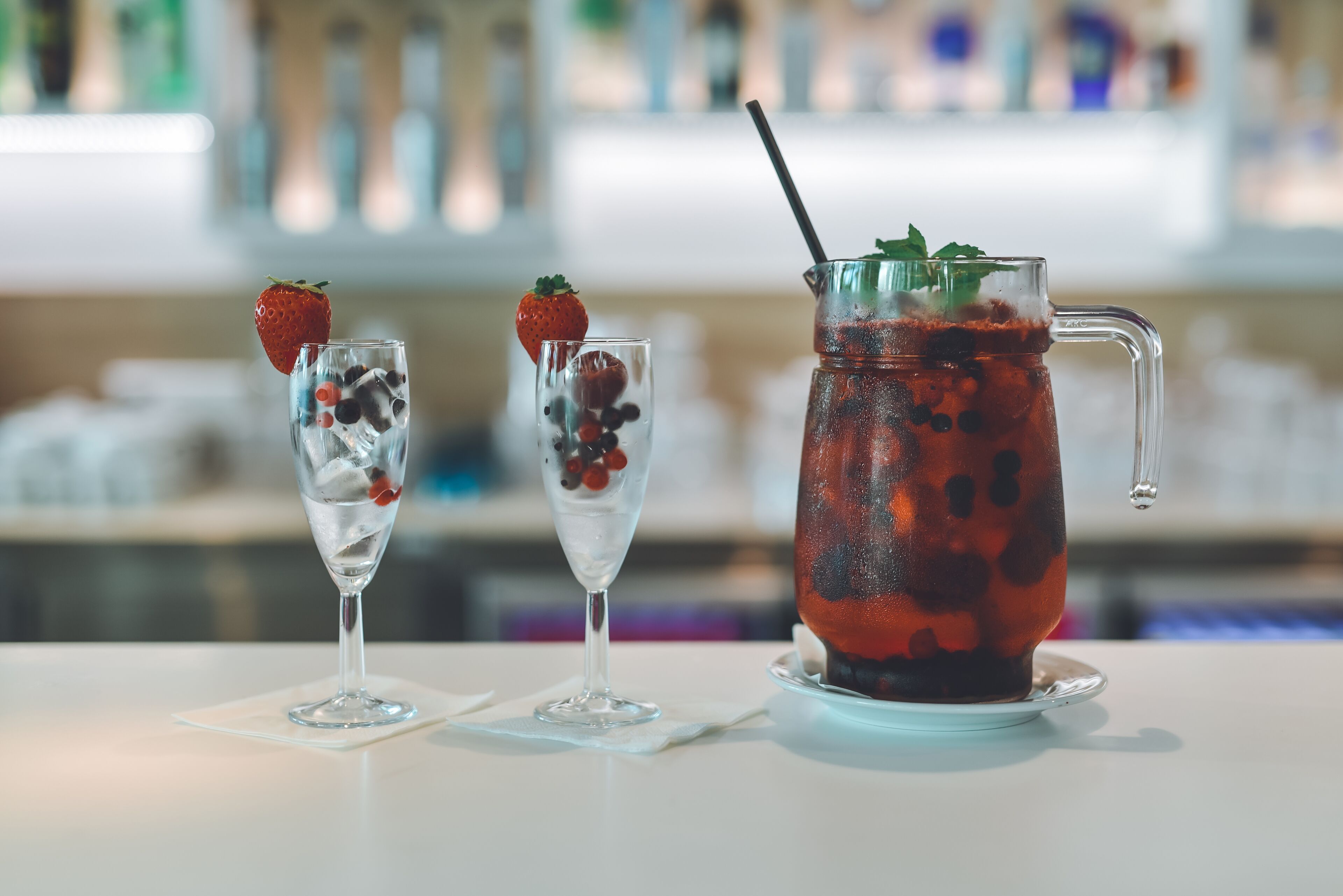 Three glasses of iced beverages with strawberries and berries, and a pitcher with a straw.