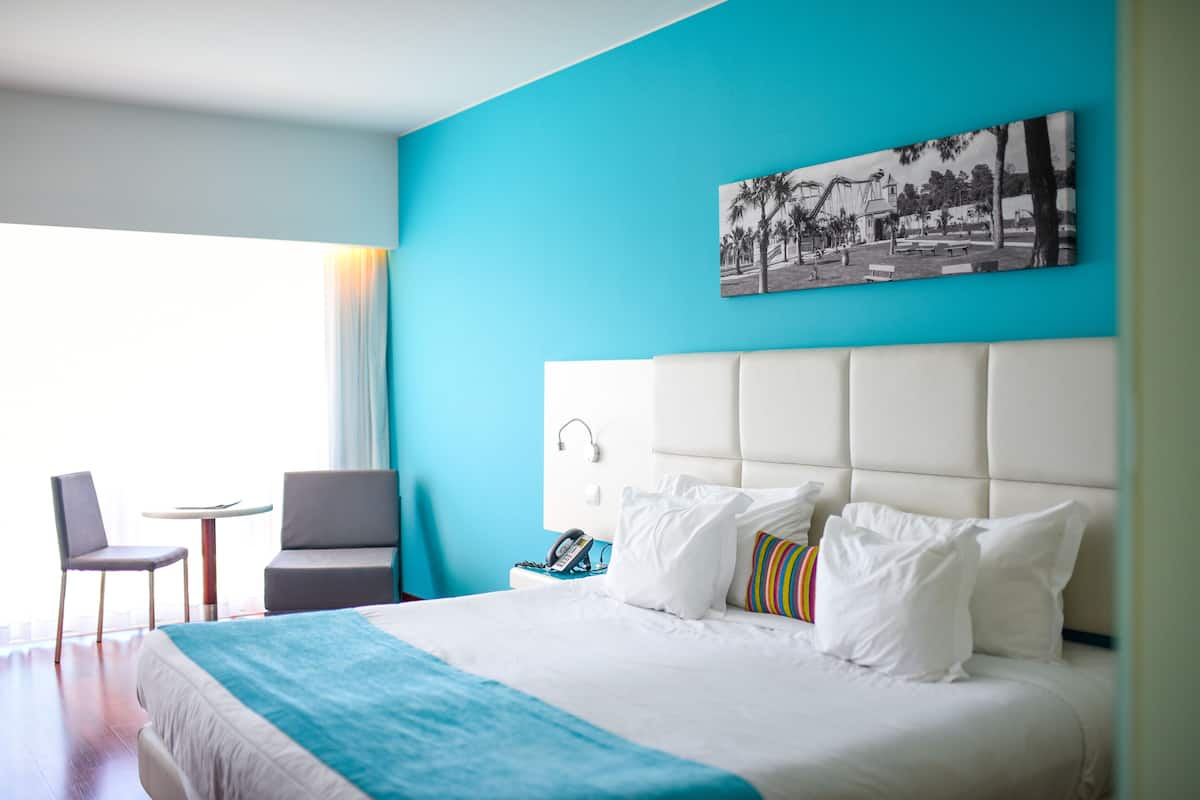 Een hotelkamer met een groot bed, een stoel, een klein tafeltje en een schilderij aan de muur.