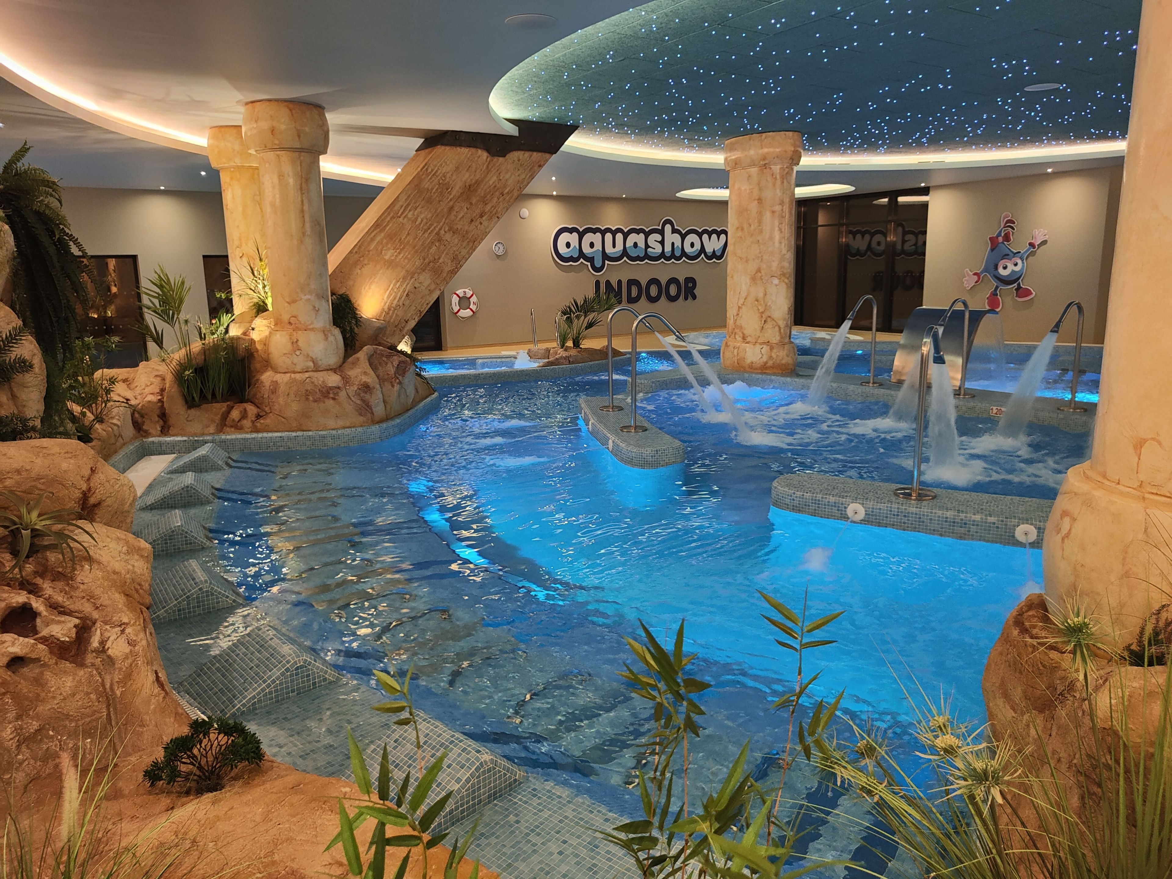 An indoor aquatic area with a pool, water features, and a sign for 'aquashow indoor.'