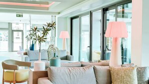 Un moderno vestíbulo de hotel con un sofá gris, sillas de madera y un amplio ventanal.