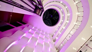 Un interior moderno con una escalera espiral, un tragaluz circular central e iluminación ambiental.
