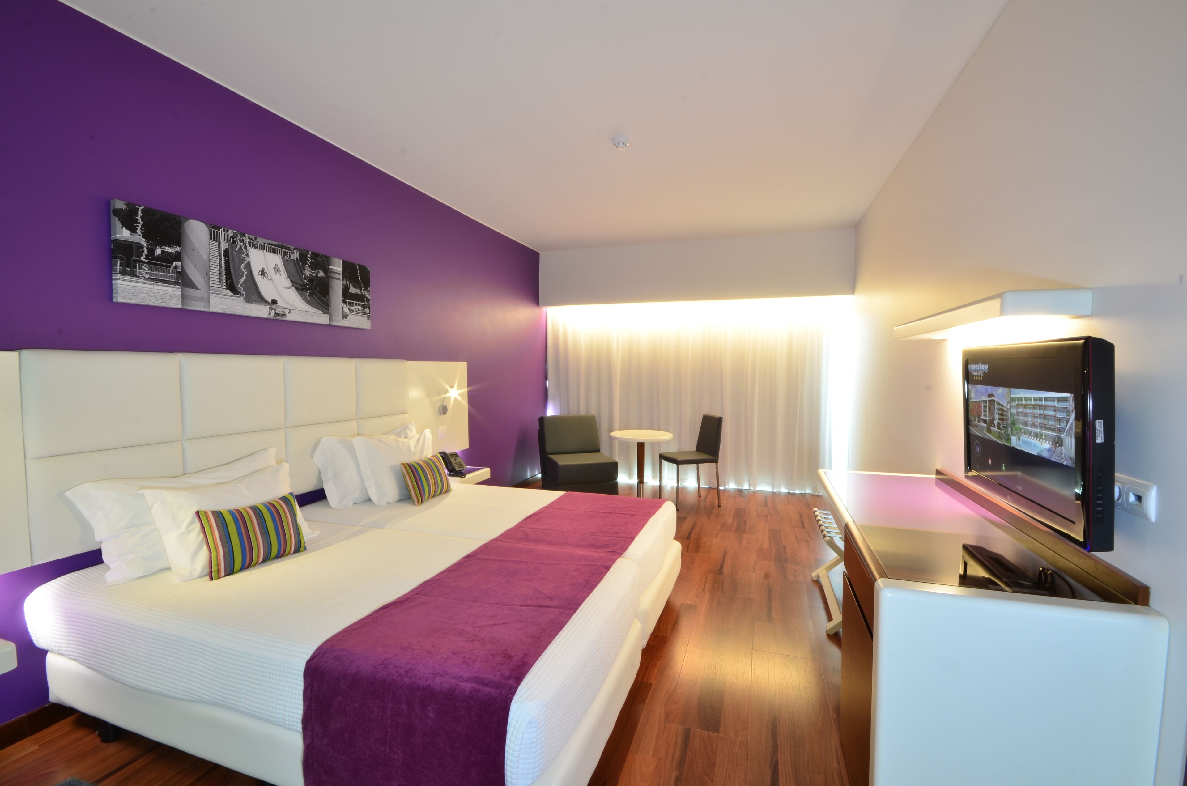 Una habitación de hotel con una cama grande, televisión, escritorio y silla.