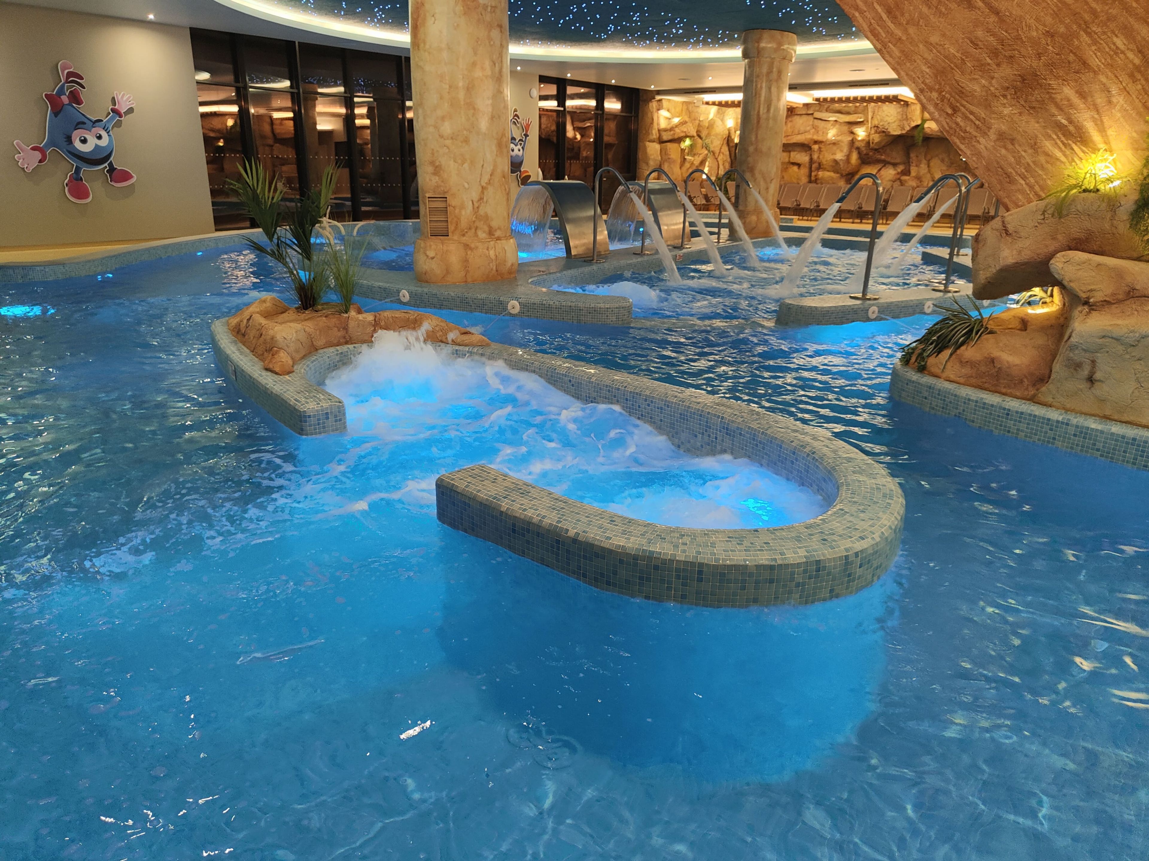 Una piscina interior con múltiples elementos acuáticos, incluyendo un jacuzzi y toboganes.