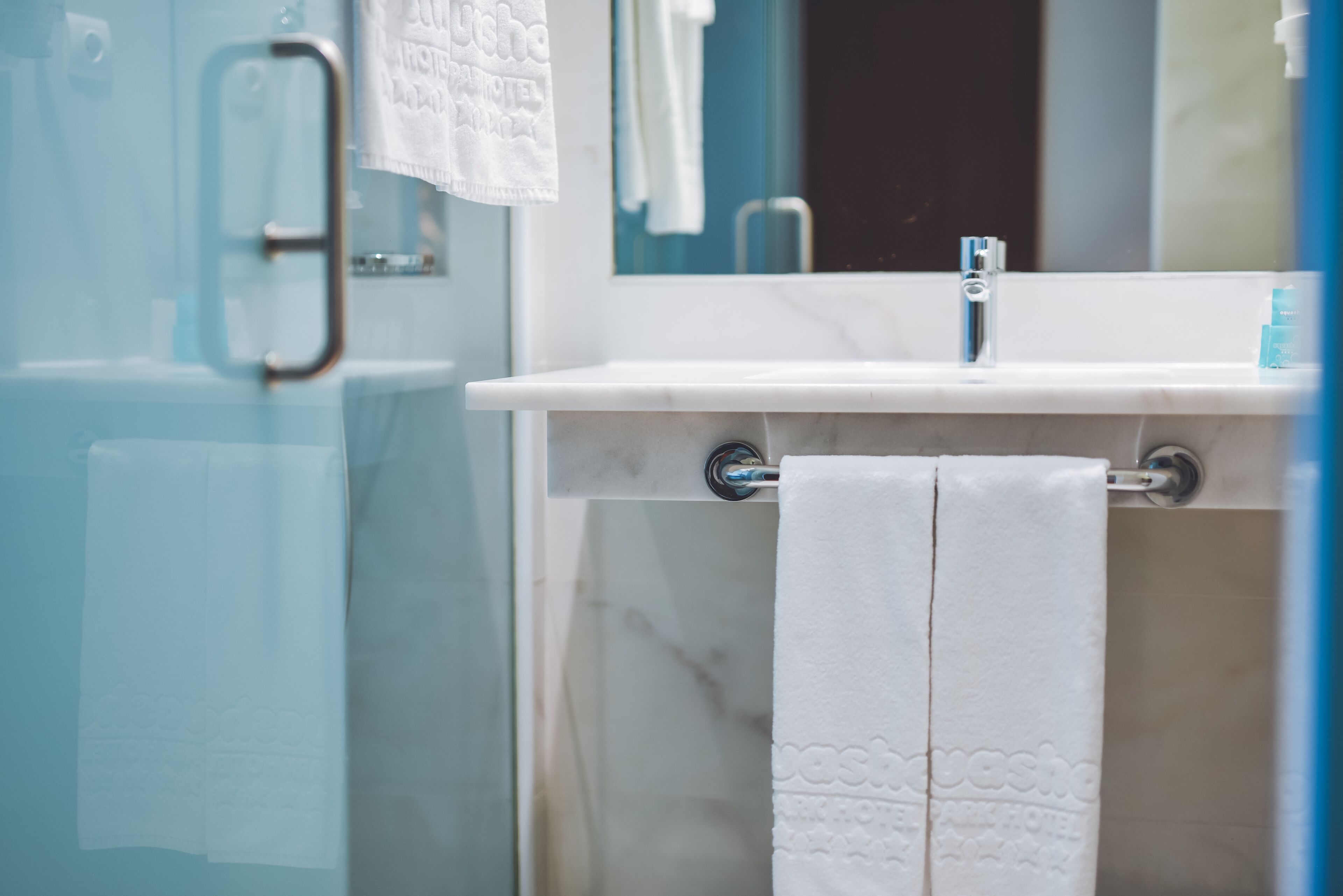 A bathroom with a glass shower enclosure, a white sink with a towel rack, and a mirror above the sink.
