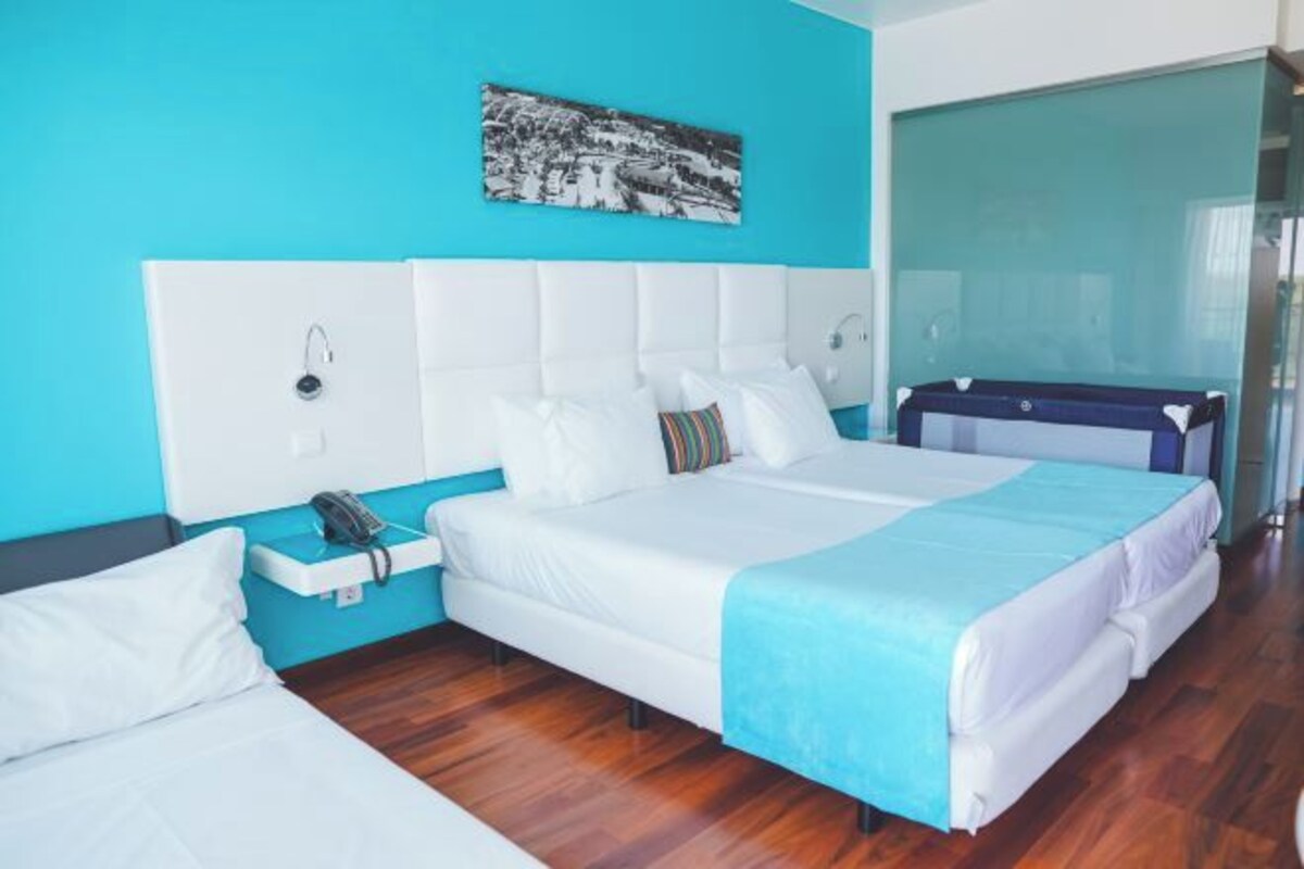 A modern hotel room with a large bed, a bedside table with a phone, and a wall-mounted light.