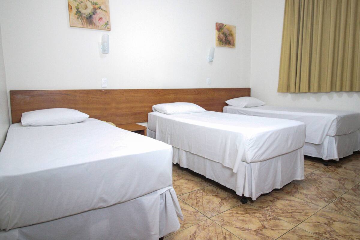 A hotel room with three single beds, a wooden headboard, a tiled floor, and two wall-mounted light switches.