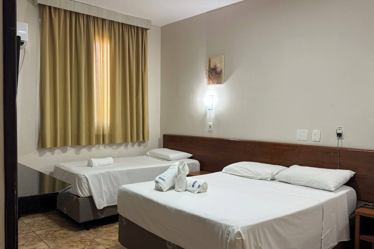 A hotel room with two beds, a wooden headboard, a wall-mounted light, and a painting.